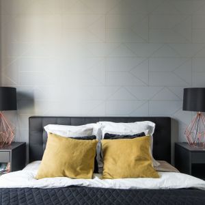 Ściana za łóżkiem w sypialni wykończona jest szarą tapetę z subtelnym, geometrycznym motywem. Projekt i zdjęcie: KODO Projekty i Realizacje Wnętrz