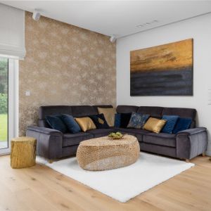Ścianę za kanapą w salonie zdobi tapeta w złotym kolorze z subtelnym, białym wzorem. Projekt: Dariusz Grabowski, Dagar Studio. Fot. Mateusz Pawelski