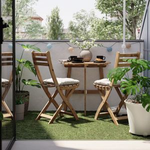 Mały balkon w bloku z drewnianymi krzesłami i sztuczną trawą. Fot. IKEA