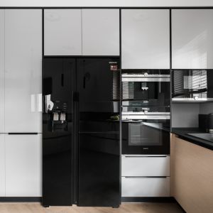 W kuchni projektanci połączyli  kolor naturalnego drewna z jasnoszarymi lakierowanymi frontami oraz lśniącymi elegancką czernią urządzeniami AGD. Projekt: Studio Projekt, Dekorian Home. Fot. Fotomohito