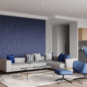 Akcenty niebieskiego (ulubionej barwy pana domu) ożywiają spokojną, neutralną kolorystykę części wypoczynkowej strefy dziennej. W takim odcieniu są poduchy na szarobeżowej, wygodnej sofie narożnej, obicie fotela i tapeta na fragmencie ściany. Projekt: Małgorzata Górska - Niwińska z Pracowni Architektonicznej MGN