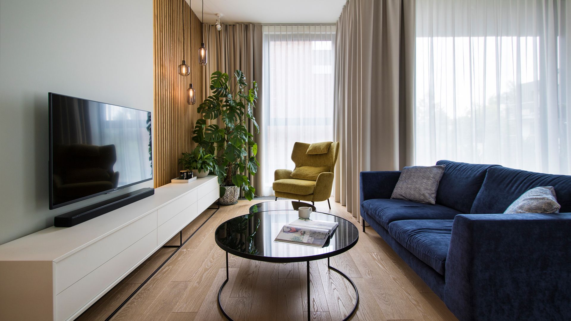 Spokojne, stonowane kolory w salonie przełamują dodatki w postaci granatowej sofy i żółtego fotela. Projekt: Natalia Teixeira, Kasia Beresińska, pracowania TK Architekci. Fot. TK Architekci