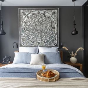 Ścianę za łóżkiem w sypialni zdobi lustro w indyjskiej, rzeźbionej ramie, które świetnie prezentuje się na tle ciemnej, szarej powierzchni. Projekt: Marta Dąbek, pracownia Interio. Zdjęcia: Pion Poziom