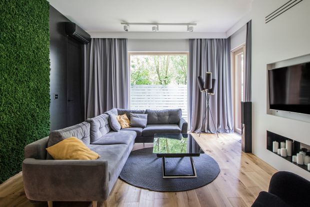 Mieszkanie o powierzchni 100 m² urządzone jest nowocześnie, ale nie minimalistycznie. We wnętrzu dominuje naturalne drewno dębowe, szarości, grafity, biel i czerń. Szalenie efektownie na ścianie w salonie prezentuje się mech chrobotek.