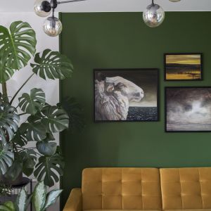 Miodowa kanapa tworzy piękny kontrast z zieloną ścianą. Projekt wnętrza: Pura Design