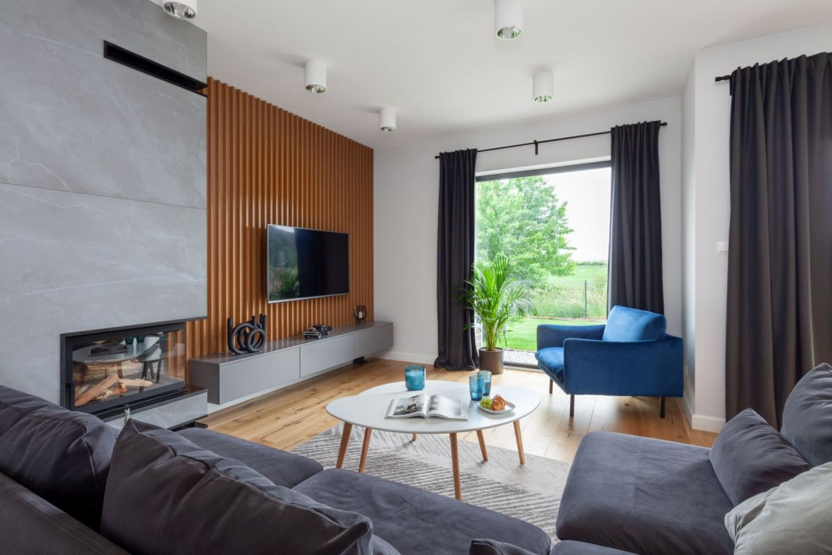 Ścianę za telewizorem wykonano z lameli drewnianych, które można zauważyć również w innych pomieszczeniach. Projekt wnętrza: Decoroom. Fot. Marek Koptyński