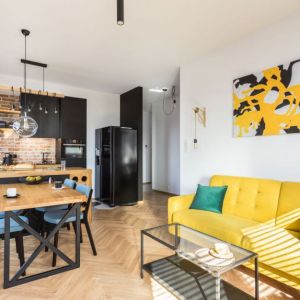 Żółta sofa w salonie, czarne meble w kuchni. Projekt wnętrza: Karolina Karwowska. Fot. Michał Młynarczyk
