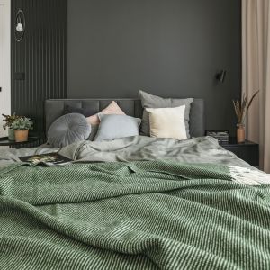 W sypialni znajduje się szerokie, wygodne tapicerowane łóżko w ciemnoszarym obiciu. Projekt wnętrza: PRW Design. Fot. Kamila Markiewicz-Lubańska. Stylizacja Maria Bartoszewska
