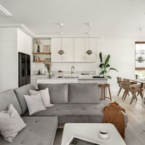 Szara kanapa w salonie, białe meble w kuchni, drewniany stół w jadalni. Projekt wnętrza: pracownia Luumo. Zdjęcie: Tom Kurek