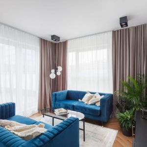Niebieskie kanapy i białe sztukaterie w nowoczesnym salonie w bloku. Projekt wnętrza: Ewa Grzywa, architekt wnętrz Decoroom. Fot. Marek Koptyński
