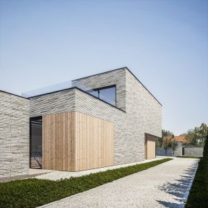 Struktura cegły jest przeplatana aluminiowymi ramami okiennymi oraz wypełnieniami w postaci okładziny z egzotycznych desek drewnianych. Projekt i wizualizacje: MEEKO Architekci