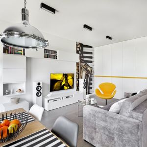 Szara kanapa i pomarańczowo-żółty fotel w małym salonie w bloku. Projekt wnętrza: Katarzyna Rohde, pracownia HOME & STYLE. Fot. Bernard Białorucki