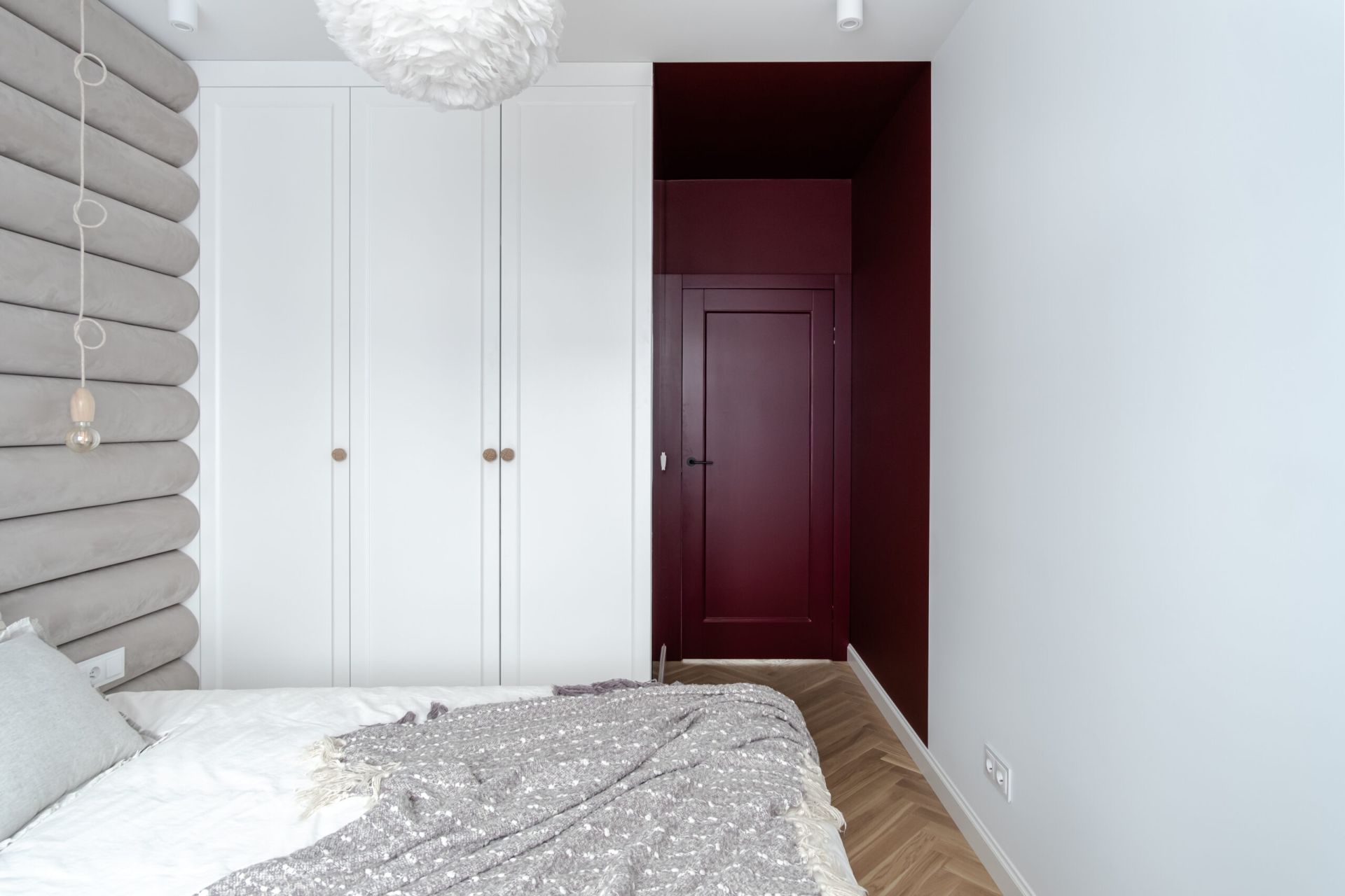 Sypialnia w bieli i kolorach ziemi, z burgundowym przejściem do łazienki. Projekt wnętrza: latreDesign. Fot. Bernadetta Kuczyńska