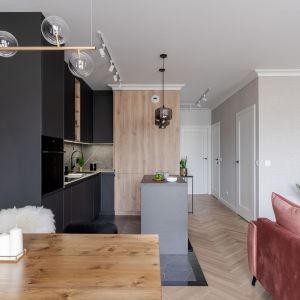 Czarna kuchnia z drewnem i małą wyspą. Projekt wnętrza: latreDesign. Fot. Bernadetta Kuczyńska