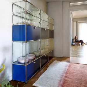 Częściowo przeszklony, a częściowo wyposażony w niebieskie fronty regał USM Haller do przechowywania zastawy stołowej. Fot. USM Haller/Mood-Design