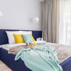 Szare ściany i niebieskie łóżko w małej sypialni. Projekt wnętrza: Decoroom. Fot. Marta Behling / Pion Poziom