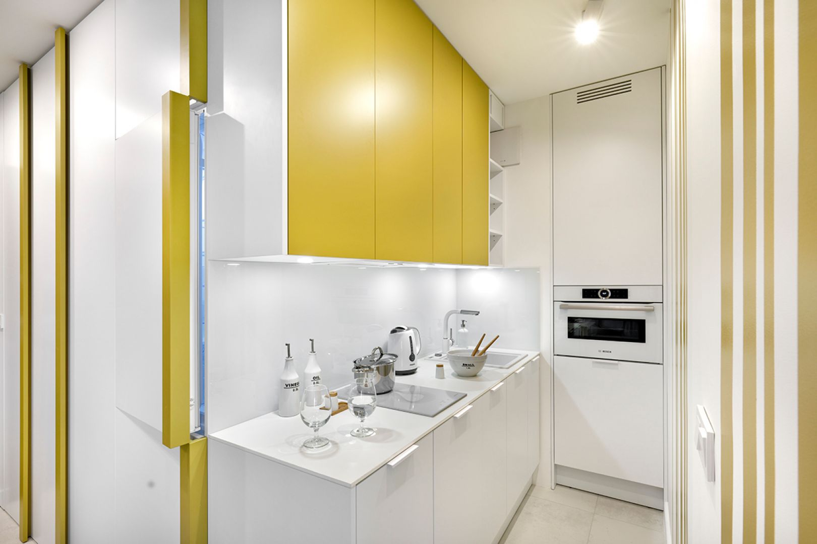 Biała kuchnia z musztardowymi frontami. 30-metrowe mieszkanie. Projekt wnętrza Katarzyna Rohde, pracownia Home&Style. Fot. Bernard Białorucki