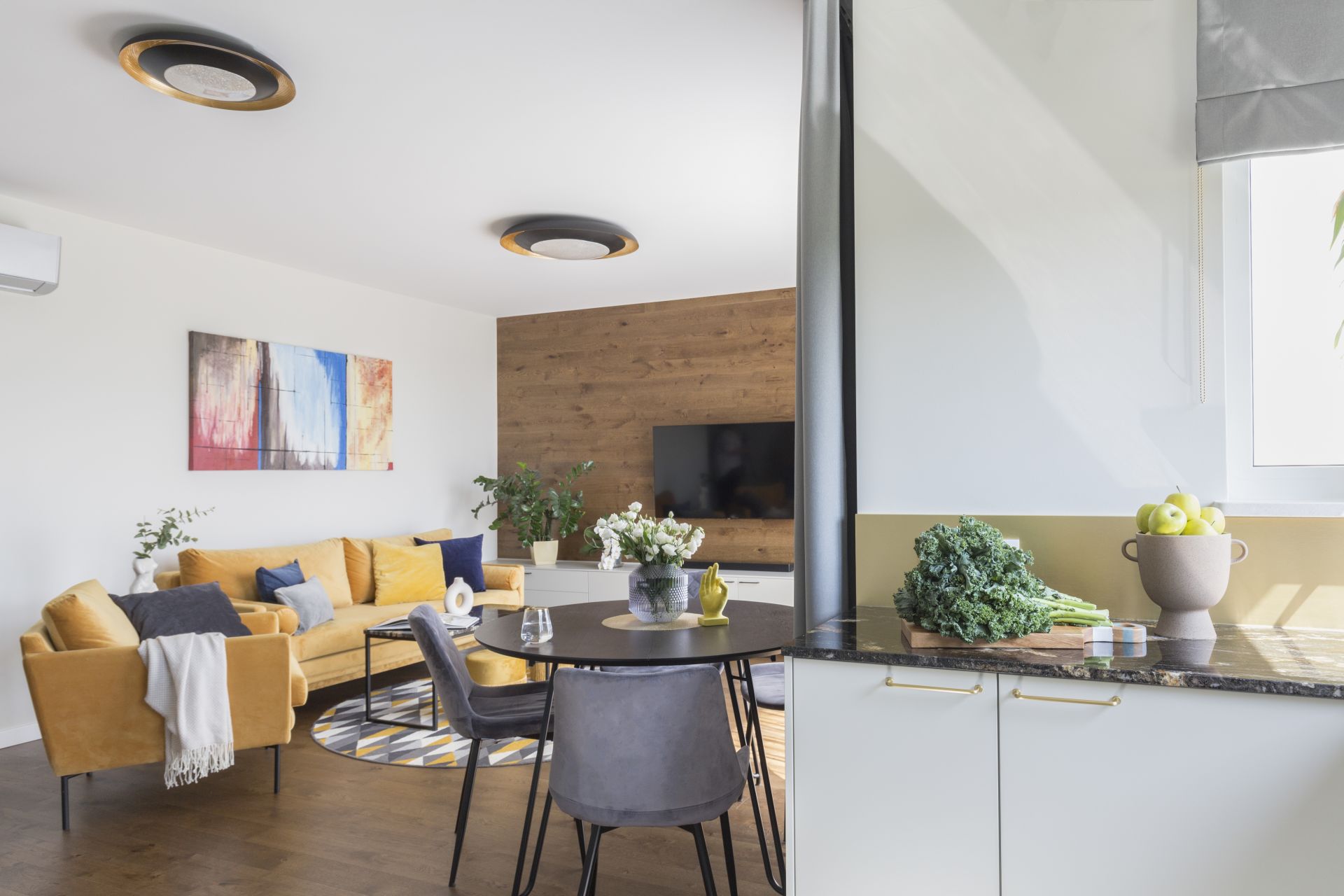 Jasny salon z musztardową kanapą i pomysłową ścianą za telewizorem. Projekt wnętrza architekt wnętrz Ewa Dziurska, Decoroom. Zdjęcia i stylizacja Marta Behling Pion Poziom