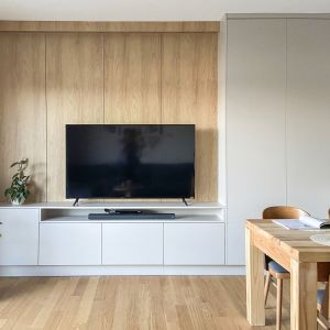 Ścianę za telewizorem w salonie zdobi jasne drewno. Projekt wnętrza: Adam Jankowski, Kamil Paszek, AMJ studio. Fot. AMJ studio