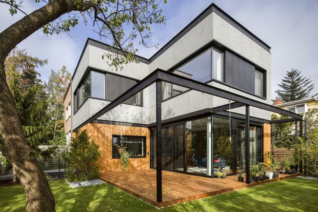 Dom jest nowoczesny i kompaktowy. Dzięki dużym przeszkleniom otwiera się na zieleń, a jego naturalny charakter podkreśla zastosowane na elewacji drewno. Architektom udało się wtopić nowy dom w istniejące otoczenie, nie ingerując w zastaną tka